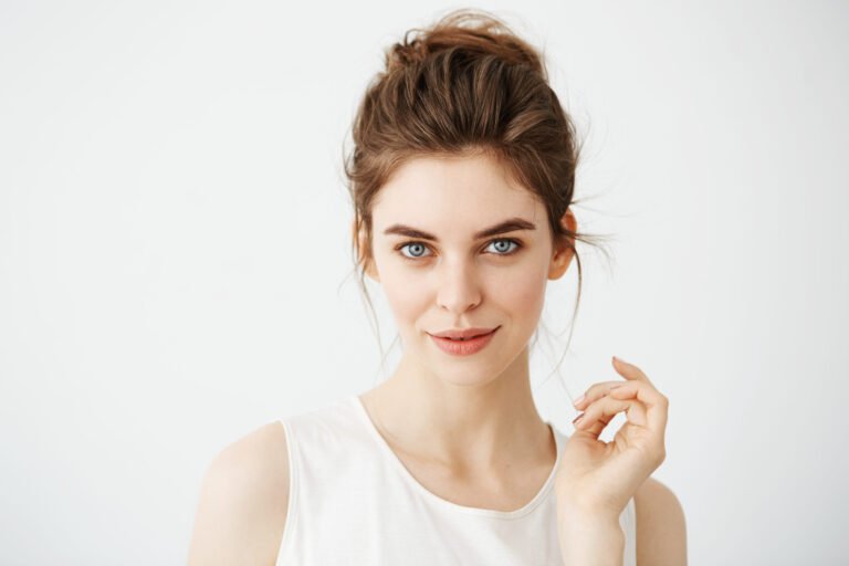 Portrait of young beautiful playful girl with bun looking at camera posing over white background